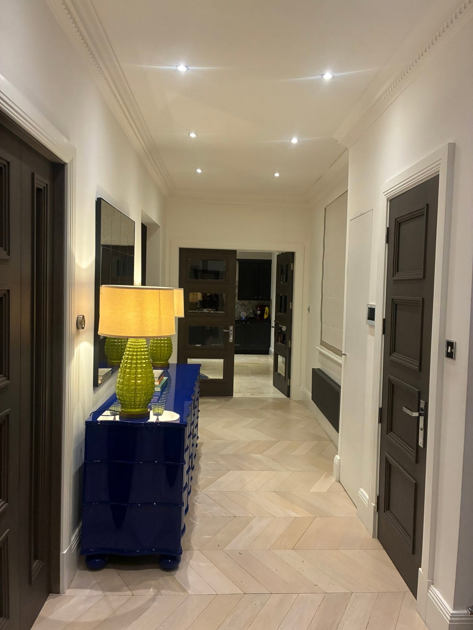 Finished hallway with painted white walls, dark doors, cornice and herringbone flooring
